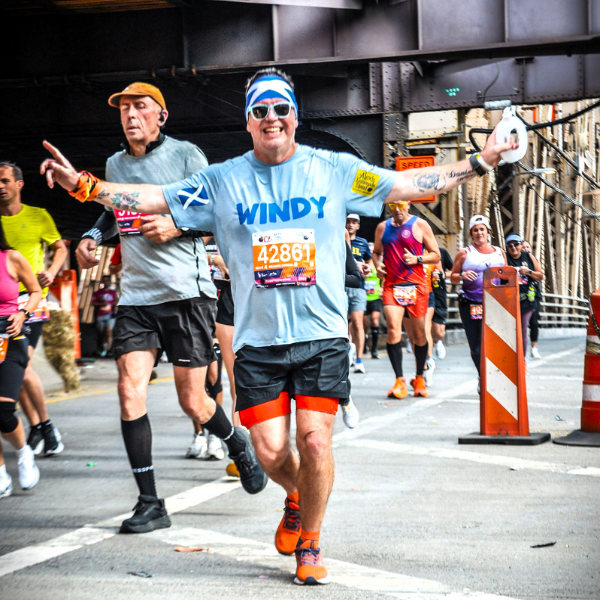 People in a running event one man in front holding his arms out smiling to the camera